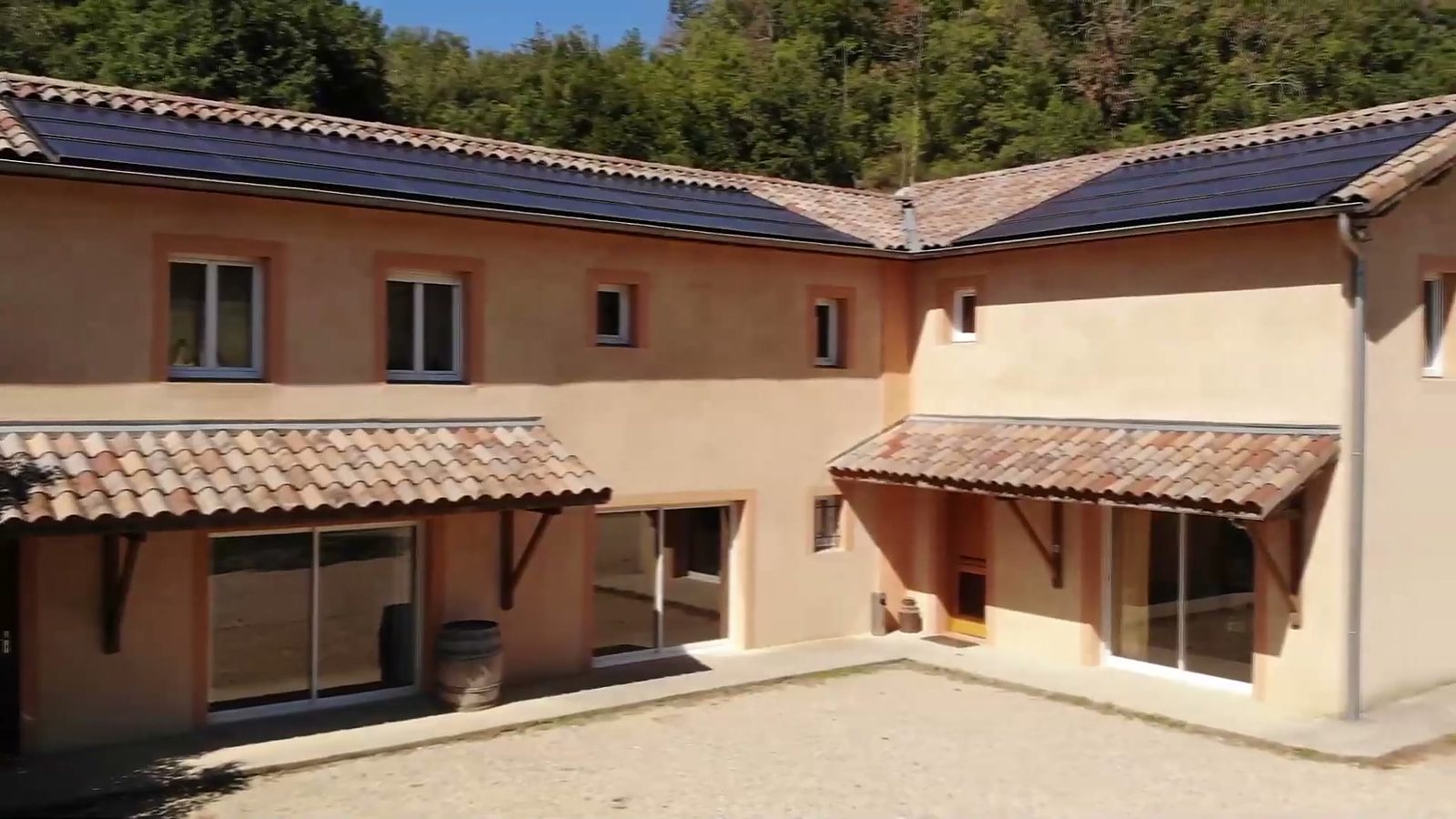 La cour des gîtes en pierre : façades ocre, auvents en tuiles et grandes baies vitrées, au soleil