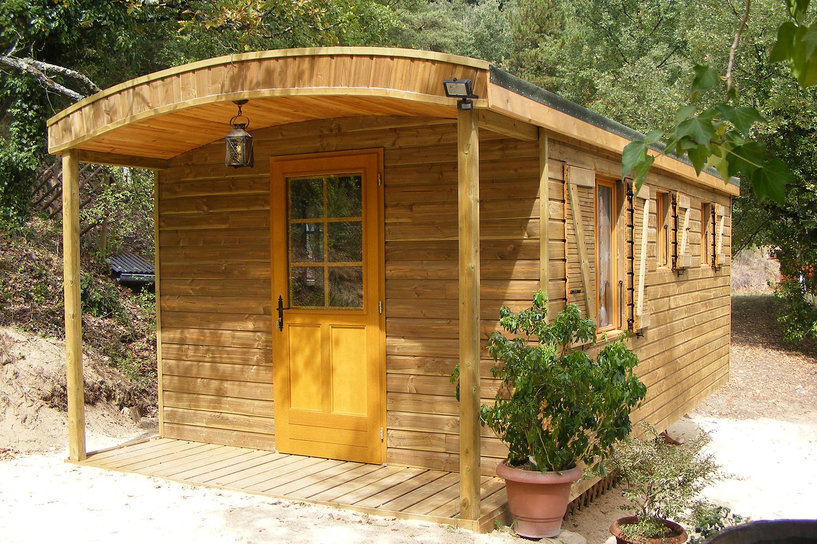 La roulotte en bois du domaine, sa porte jaune et sa petite terrasse, sous les arbres