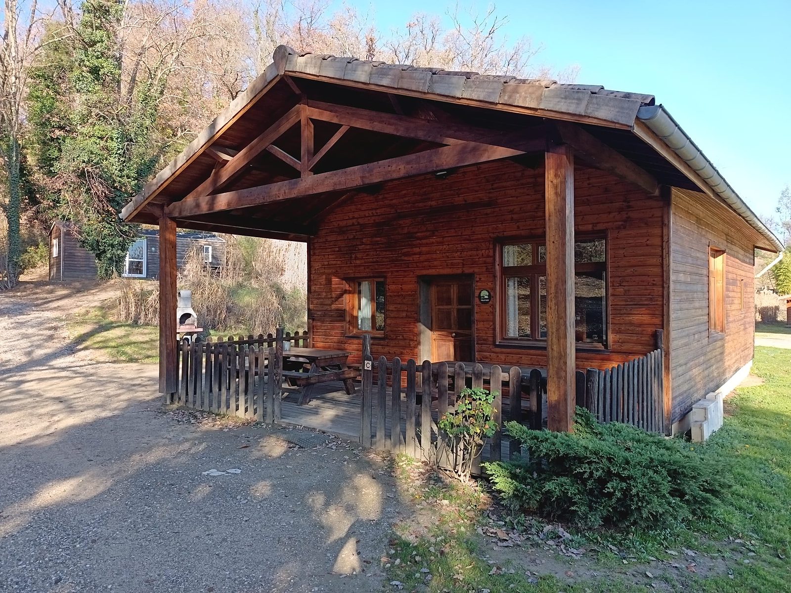 Le chalet Truffier en bois, sa grande terrasse couverte et sa barrière, au soleil d'hiver