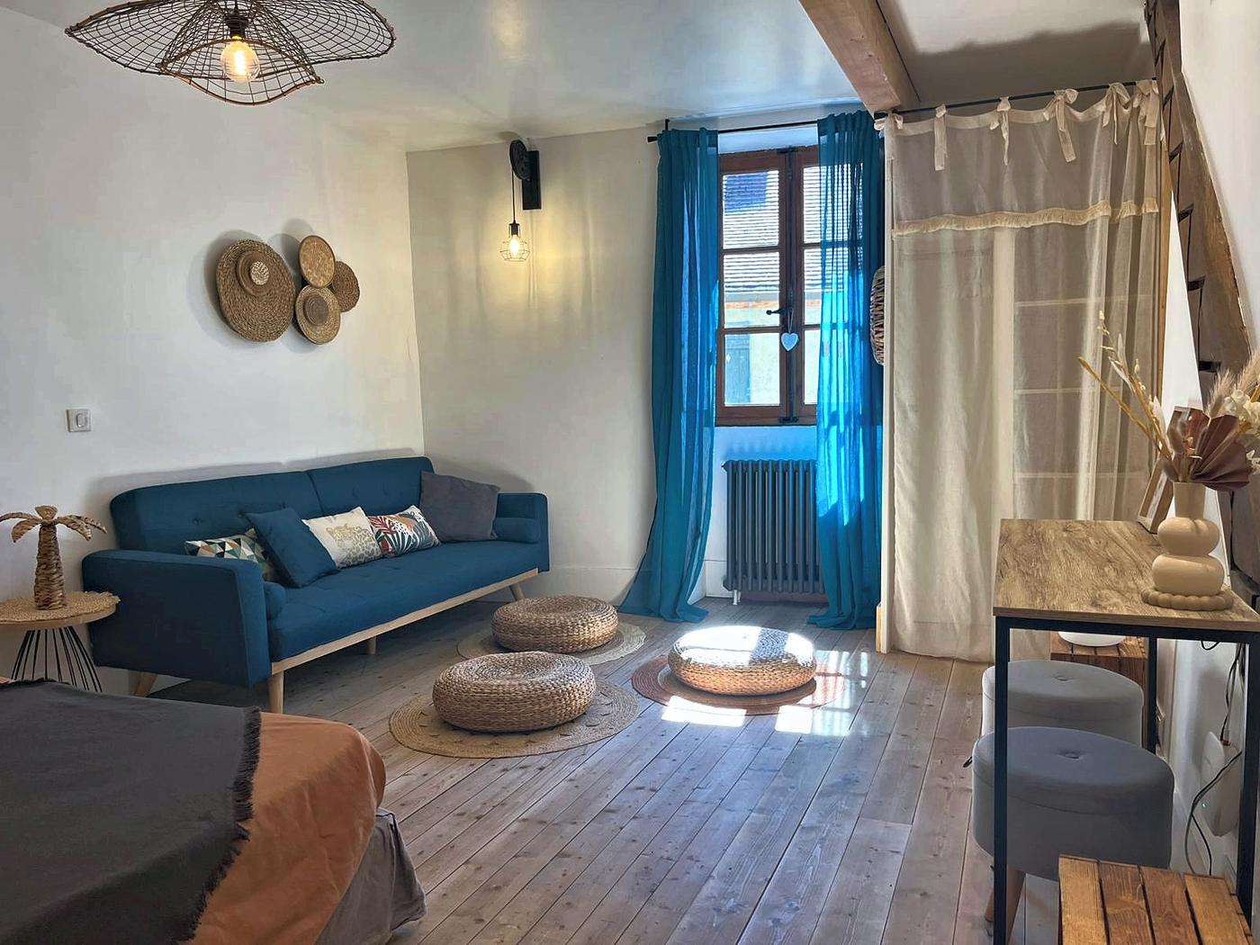 Le salon de La Mercantine : canapé bleu, fenêtre à volets et poufs